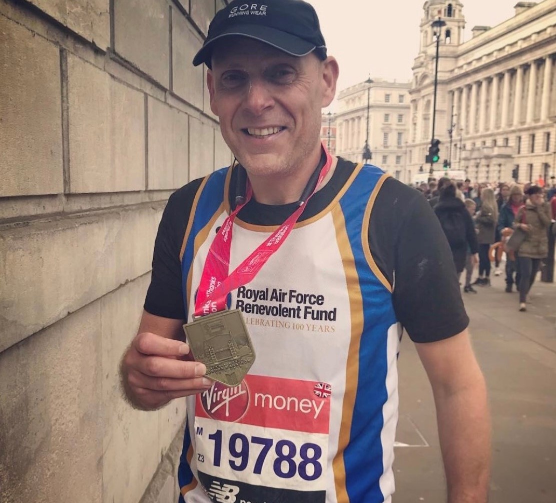 Carl is smiling, and wears a London Marathon medal which he is holds up to the camera. His running vest reads Royal Air Force Benevolent Fund.