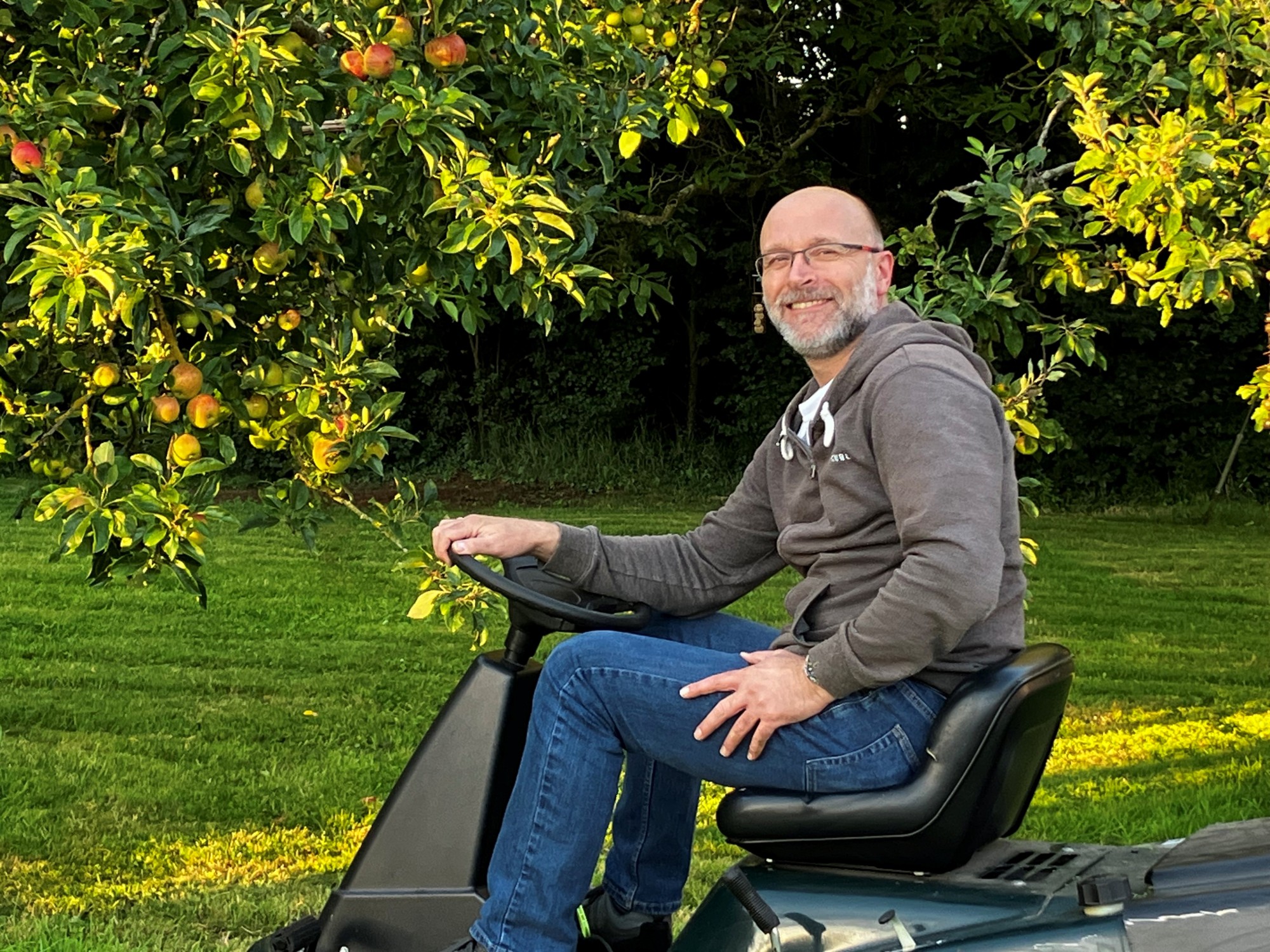 Graeme is pictured on a lawn mower with an orchard behind him.